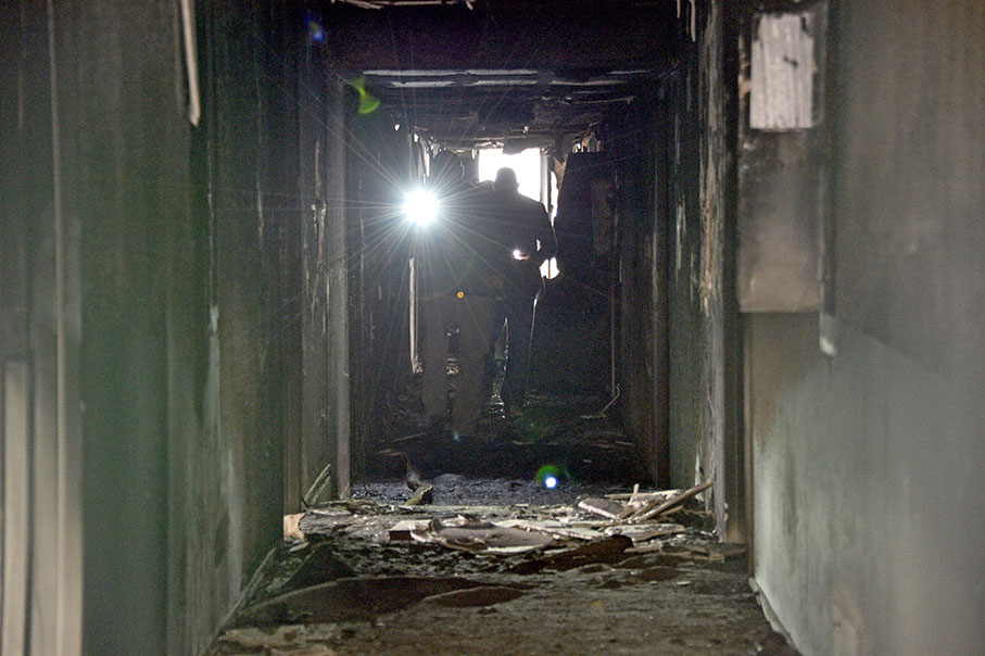 火势扑灭后，消防员周六在公寓外聚集，可见公寓部分外墙被熏黑。（美联社）