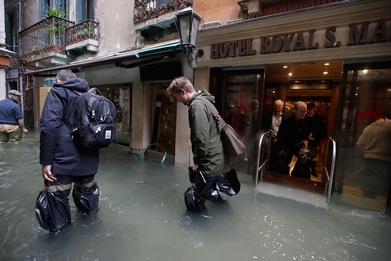 威尼斯被洪水围困，路人经过酒店时需小心步行，涉水而过。（美联社）