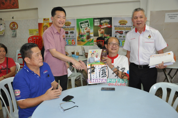 谢琪清（站者左）派发月历给用餐的市民。 