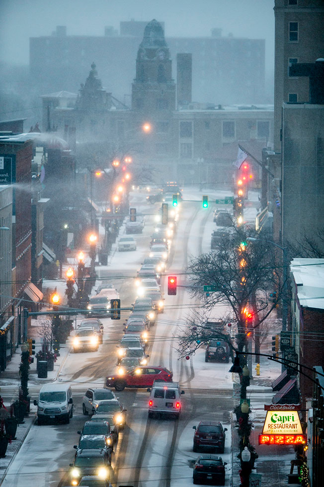 美国伊利诺伊州罗克福德市周六被白雪覆盖，车辆开启大灯缓慢行驶。（美联社）