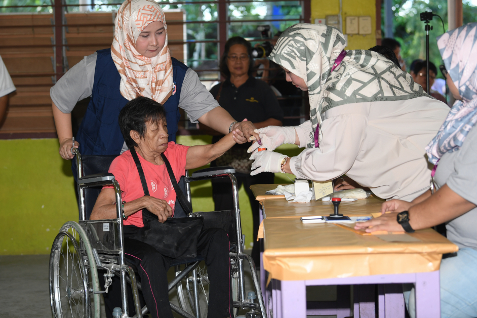 投票中心工作人员为坐在轮椅上的露欣玛达吉（左）的手指沾上墨汁，表示已经履行公民义务。