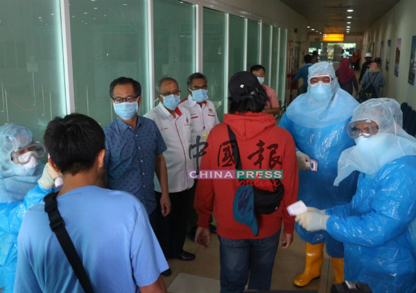 穿上太空装的官员为抵达机场的乘客测量体温，左3为刘志良。