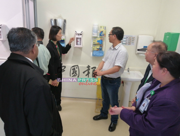 陈秋花（左3起）向刘志良讲解院方提供的自动式消毒洗手液。
