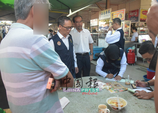 烟民（左起）在刘志良及阿米鲁拉等面前，看着执法员发出罚单。