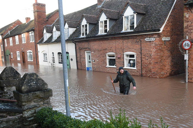 英国西部滕伯里威尔斯特梅河决堤造成街道淹水，一名男子周日涉水越过道路。（法新社）