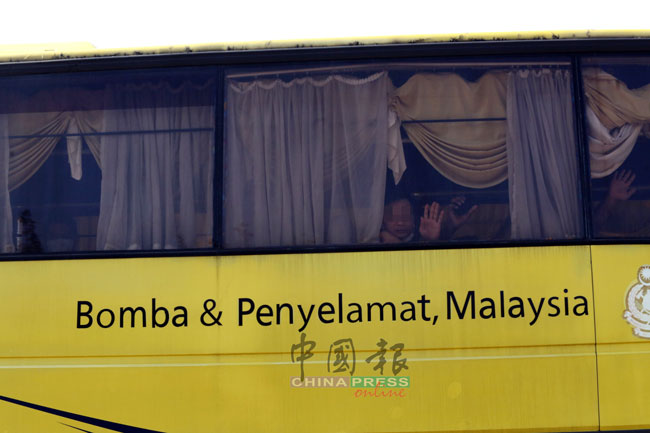 巴士上的回国者向摄影记者挥手。
