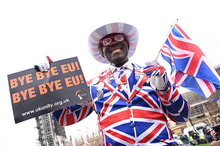 民众穿着“英国国旗”衣服，在伦敦国会大厦对面的议会广场上，举着“再见欧盟”的标语。（法新社）