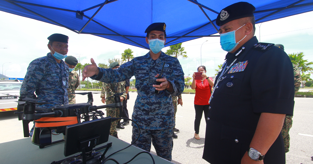 阿都加里尔（右）在丹绒隆坡行动管制军警路障中心，向空军祖海利（中）了解扩音广播无人机的操作流程。