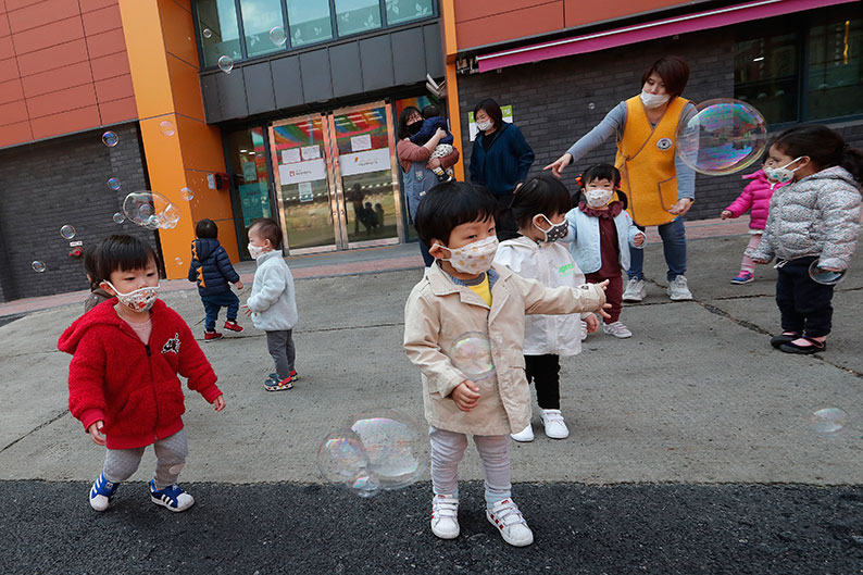 戴着口罩的一群儿童在大人陪同下，周五在首尔的曹溪寺外开心玩泡泡。（美联社）