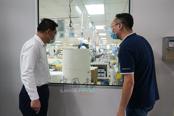 林万锋（左）向王昌林了解口罩的生产情况。
