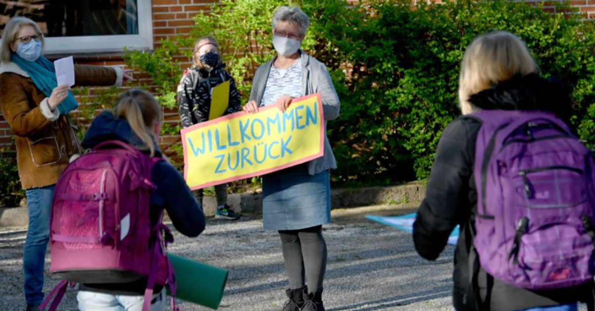 在石勒苏益格-荷尔斯泰因州，一名老师在6日于学校门口举牌，欢迎学生返校。