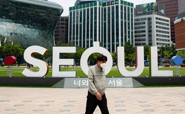 韩国一名戴口罩的男子，周二徒步经过首尔市政厅大楼。（图：欧新社）