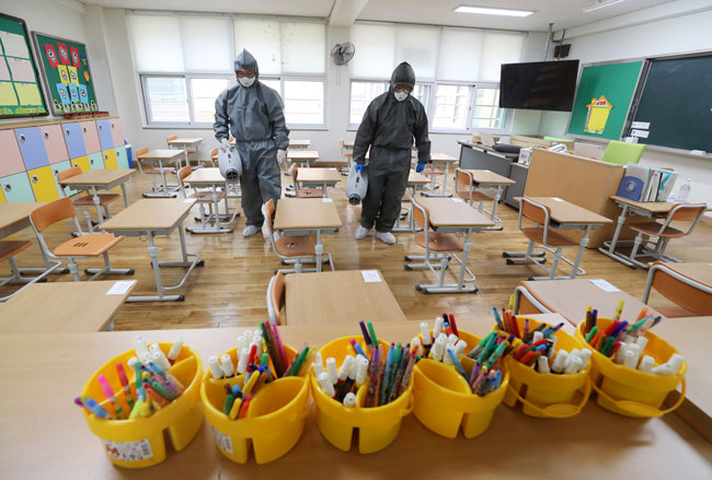 身穿防护服的工作人员，周二在韩国光州市的一所小学课室内进行消毒工作。（图：美联社）