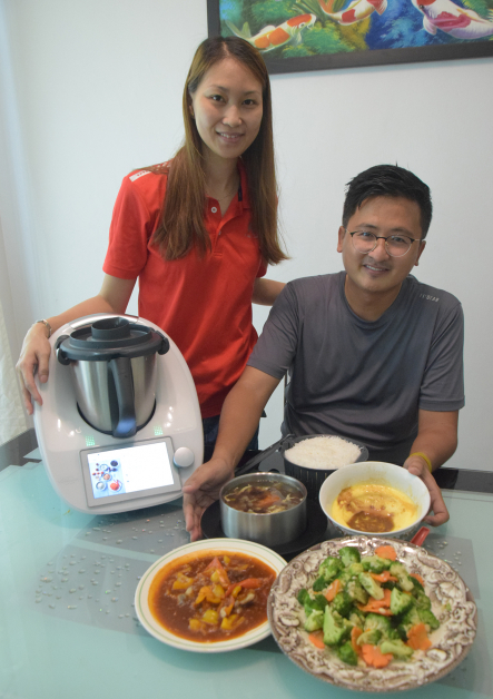 谢守钦（坐者）在李秀萍教导使用小美万能机下，煮出健康又美味的三菜一汤。