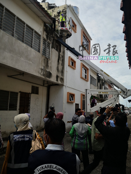 卫生局官员动用云梯，爬到商店的屋顶检查积水。