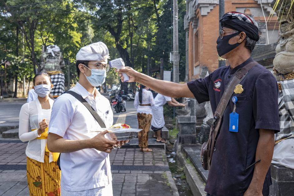 峇厘岛民众4日庆祝萨拉斯瓦蒂节，当地传统保安巡逻人员为进入庙宇的信徒测量体温。（欧新社）