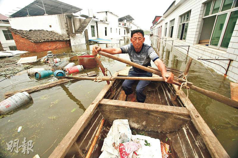 村民周先生划着小艇，在被水淹的村中打捞店中被冲出的货物。水中可见到漂浮的石油气桶、门板及垃圾。（明报）