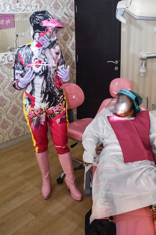 在中爪哇省玛琅，女牙医奥古斯汀（左）舍弃一般的防护装备，换上特别订制的花样防护装。她说，这套服装除了有防疫作用，也有助分散病人紧张情绪。（法新社）
