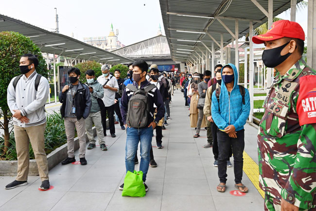 在印尼茂物市一火车站，在保安人员的监控下，人们戴着口罩、保持安全距离排队，等候去耶加达的列车。（法新社）