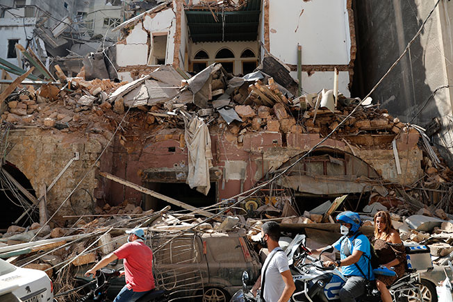 贝鲁特市民周三骑摩哆经过被爆炸破坏损毁的屋子。（美联社）