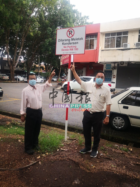 汉都亚再也市议会在大树下设乱泊车罚款100令吉的告示牌，提醒车主。左起为黄罗玖（左）和叶汉良。