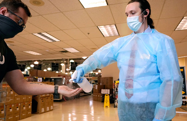 美国达拉斯一间电脑店的员工，在为身穿防护服的顾客进行消毒工作。（美联社）