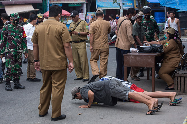 周三在印尼棉兰，2名违反防疫规定的男子被官员处罚掌上压。（美联社）