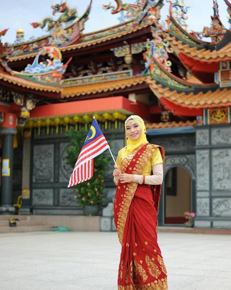 马来少女身穿纱丽，在神庙前挥舞国旗拍照。 