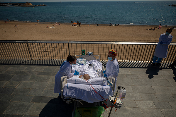 西班牙巴塞罗那海边的德尔马医院施行“人道”加护病房计划，让新冠肺炎患者可以到海滩享受10分钟空气与阳光。（美联社）
