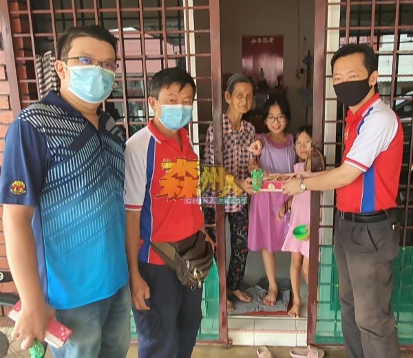 谢琪清(右)为老幼村民递上月饼和猪仔饼,让年幼的孩子品尝猪仔饼的味道,左起为李汉强和李恒华。