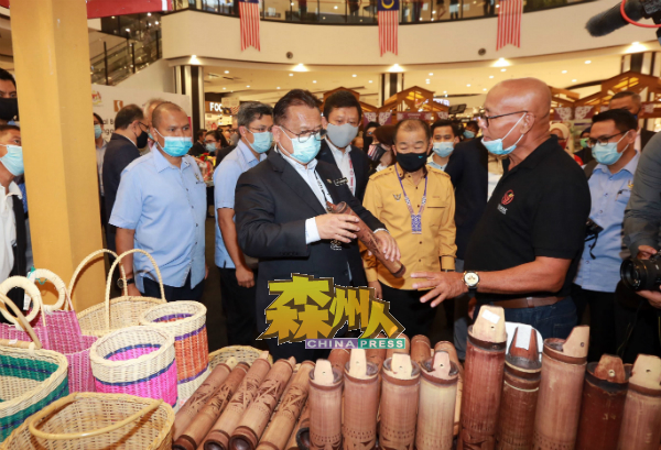 嘉年华会销售砂州各式的手工艺品,令人眼前一亮,业者在阿历山大(左)巡视展销位摊位时讲解商品特点。