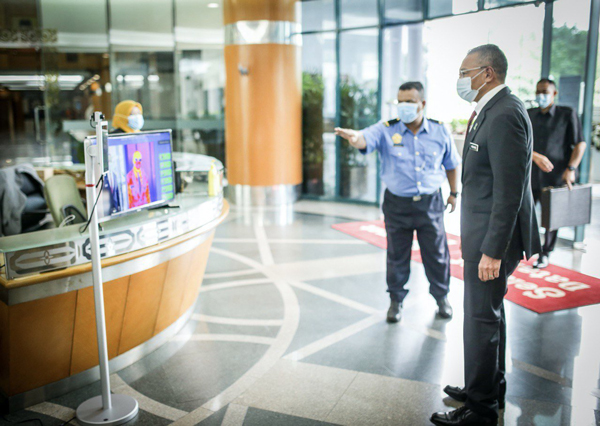 希山慕丁（右）周二回到外交部办公时，在入口处的红外线体温测量仪前量体温。