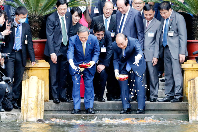 日本首相菅义伟（前左）和越南总理阮春福（前右），周一在河内主席府内的池塘洒饲料喂鱼。（欧新社）