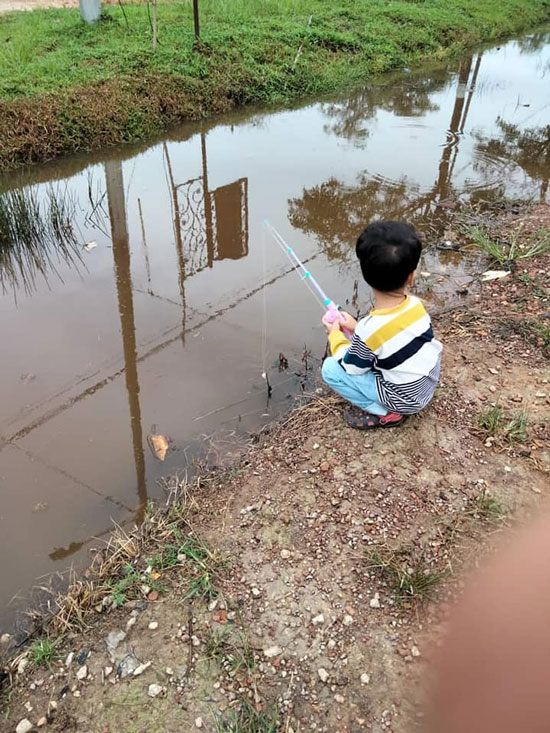 3岁男童用莫哈末法雅以玩具钓竿，在沟边垂钓。