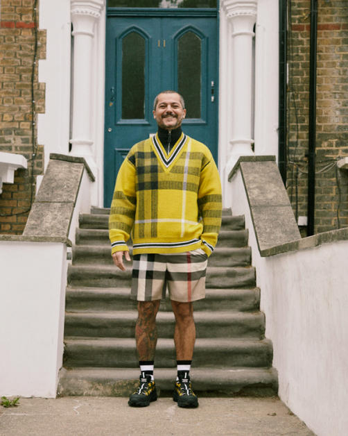 Burberry配件设计师Massimo穿2021早春格纹毛衣与短裤在位于Hackney自家门口拍型录。