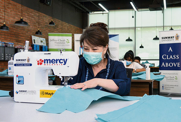 在疫情期间，双威大学与大马医药援助协会（MERCY ）合作开展了个人防护设备（PPE） 缝纫项目，图为双威的学生和校友志愿者参与其中，而李馥彦博士亦尝试缝制个人防护装备。