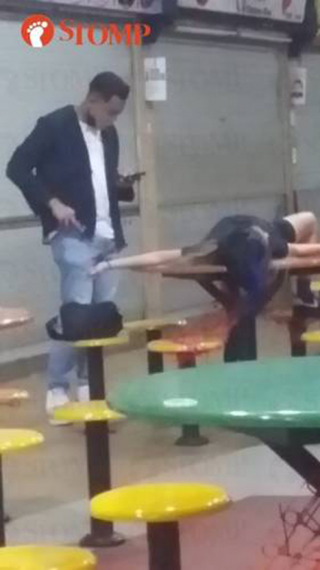 女子醉卧在美食中心的桌子上，身旁有一名男子在滑手机。（取自网站“Stomp”）