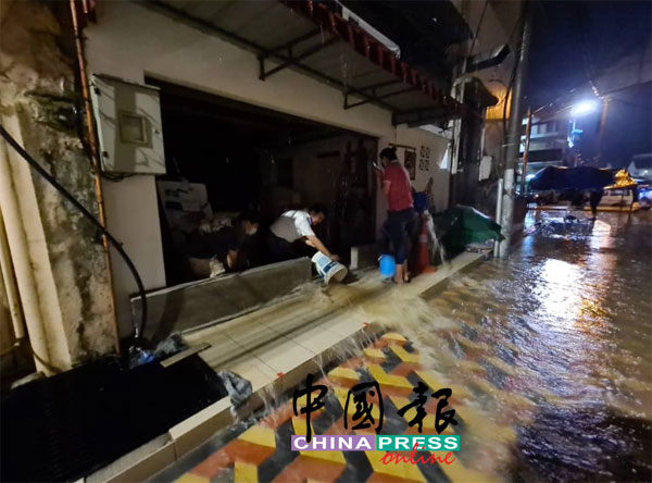 商家忙于用水桶，将店里的积水倒出路旁。