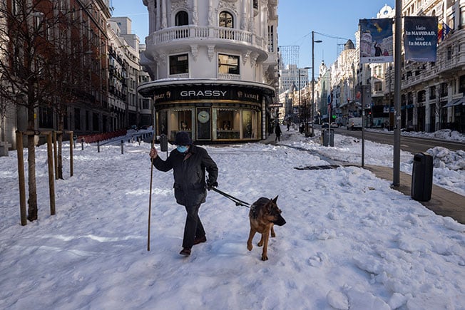 一名拄着拐杖的男子牵着一只狗，在马德里的雪地行走。（美联社）