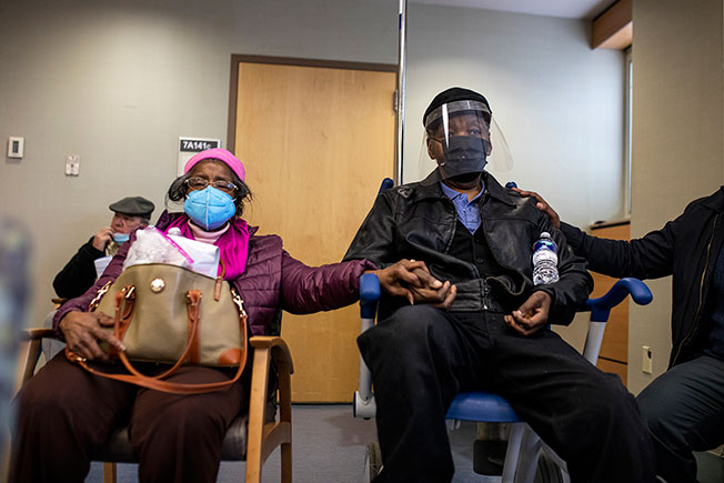 费城一名男子接种疫苗后在观察室休息，其妻子握着他的手表达关爱。（美联社）