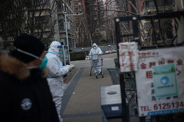 周三在北京大兴融汇社区南门，穿着防护服的工作人员准备用小推车运送物资。（新华社）