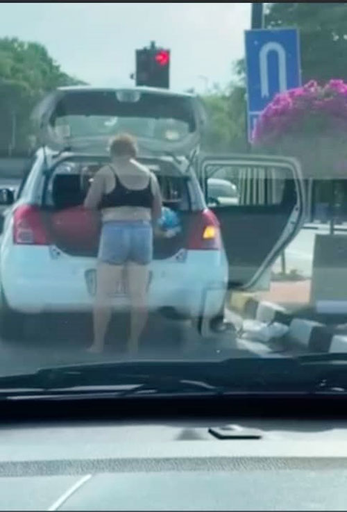 妇女打开车后厢，准备把车上物件抛到路上。