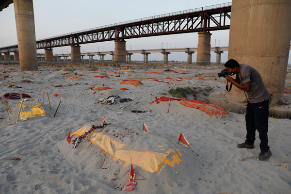周六在印度北方州普拉亚格拉杰桑加姆地区，恒河岸边的沙滩上出现多具浅埋遗体，一名男子在现场拍摄。（美联社）