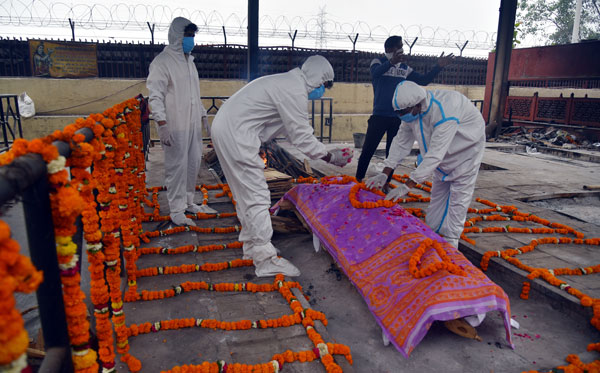 在新德里，全副防护装的工作人员在处理一具新冠死者的遗体。（欧新社）