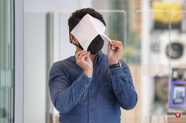 被告张旻轩走出庭外时， 用一张白纸遮住自己的脸。（海峡时报）