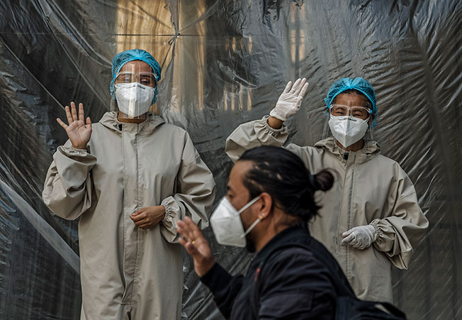 在尼泊尔加德满都的一所隔离中心，身穿防护衣的医护人员向离开隔离中心的新冠肺炎康复病人挥手致意。（欧新社）