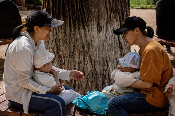 5月25日，有两名妇女抱着自己的孩子，在北京一处公园聊天。（法新社）