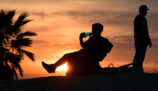美国加州洛杉矶迎来热浪天气，图为一名儿童在洛杉矶欣赏夕阳时喝水。（法新社）