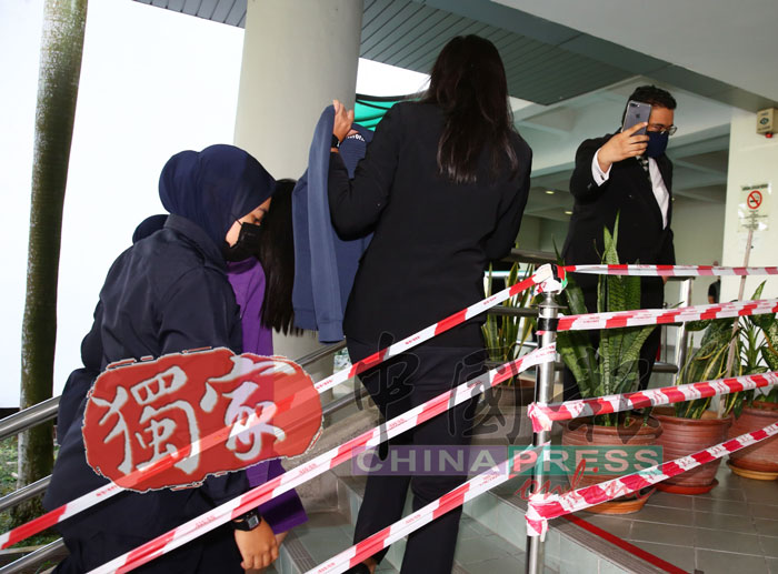 女嫌犯代表律师一路以衣服为其遮挡摄影记者的镜头。