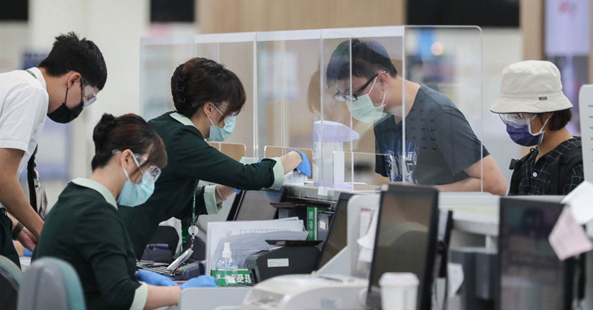 地勤人员周五在台北松山机场为旅客办理登机手续，柜台架设防疫透明隔板，希望降低病毒传播风险。（中央社）